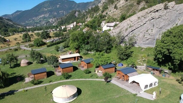 Une yourte, plusieurs yourtes et une tente blanche dans une zone herbeuse, avec une chaîne de montagnes en arrière-plan.