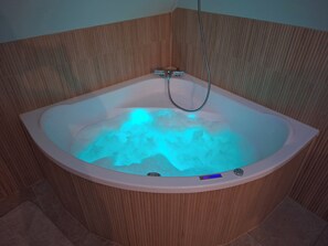 A corner bathtub with a shower head, a control panel, and a wooden panel wall.