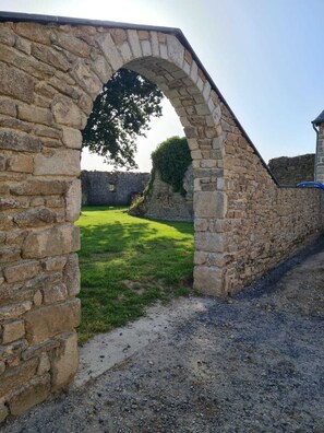 A stone archway leading to a grassy area with a stone wall and a building in the background.
