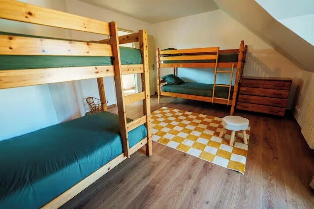 A room with two bunk beds, a wooden dresser, a checkered rug, and a small stool.