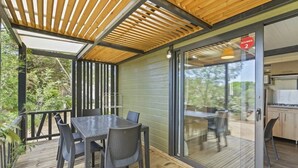 Un espace extérieur abrité, doté d’une table et de chaises, une porte-fenêtre coulissante donnant sur une cuisine et une terrasse en bois.