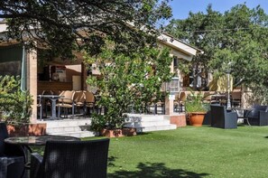 Une terrasse extérieure aménagée avec des meubles en osier, une cheminée en pierre et une pelouse bien entretenue.