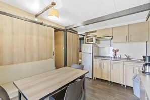 Ett modernt kök med träskåp, ett matbord, stolar, en mikrovågsugn, ett kylskåp och en spis.