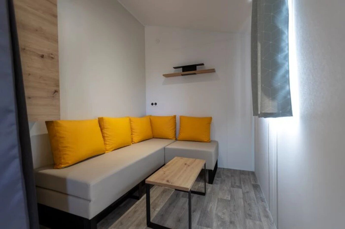 Un salon moderne avec un canapé d’angle, une petite table en bois et une étagère intégrée.