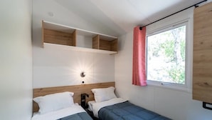 A small room with two beds, a wooden headboard, a wall-mounted shelf, a window with a curtain, and a wall light. - Camping 3 étoiles - Piscine  - ccbgebe (Pianottoli-Caldarello)
