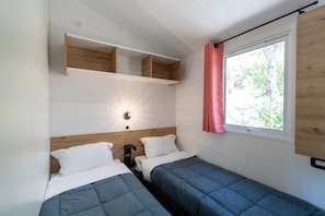 A small room with two beds, a wooden headboard, a wall-mounted shelf, a window with a curtain, and a wall light. - Camping 3 étoiles - Piscine  - ccbgebe (Pianottoli-Caldarello)