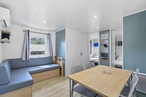 A modern room with a sofa, a dining table, and a bed in the background. - Camping 3 étoiles - Piscine  - ccbgebf (Pianottoli-Caldarello)