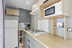 A compact kitchen with a built-in gas stove, a microwave, and a coffee maker. - Camping 3 étoiles - Piscine  - ccbgebf (Pianottoli-Caldarello)