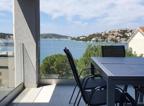 Ein Balkon mit Tisch und Stühlen, der Blick auf ein Gewässer und eine Hügelstadt freigibt.