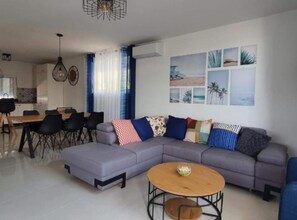 Ein modernes Wohnzimmer mit einem grauen Ecksofa, einem runden Couchtisch und einem Essbereich mit Tisch und Stühlen.
