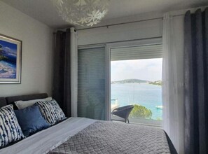 Ein Schlafzimmer mit Bett, einem Gemälde, Meerblick und einem fenster mit Vorhängen.