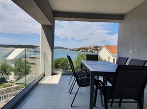 Ein Balkon mit Tisch und Stühlen, der auf ein Gewässer und eine ferne Stadt blickt.