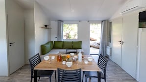 A dining area with a table set for four, a green cushioned bench, and a view through a window. - Camping 3 étoiles - Piscine  - ccbgebh (Pianottoli-Caldarello)