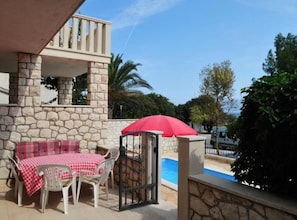 Ein Steinhaus mit Balkon, Pool und Sitzgelegenheit mit rotem Sonnenschirm.