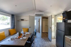 A modern kitchen with a dining area, a built-in oven, and a view through an open door. - Camping 3 étoiles - Piscine  - ccbgebi (Pianottoli-Caldarello)