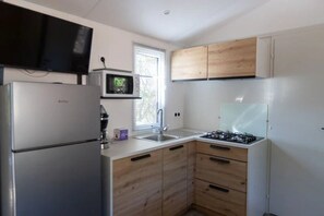 A compact kitchen with a refrigerator, microwave, stove, and wooden cabinets. - Camping 3 étoiles - Piscine  - ccbgebi (Pianottoli-Caldarello)