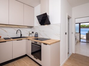 A modern kitchen with a built-in oven, a coffee maker, and a kettle on the countertop. - One Bedroom Apartment with Terrace and SeaView(A3) (Omis)