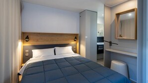 Een moderne hotelkamer met een groot bed, een houten hoofdbord, nachtlampjes, een inbouwkast en een spiegel aan de muur.