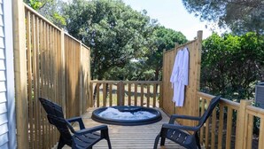 Een houten terras met een jacuzzi, twee stoelen en een handdoekhouder.