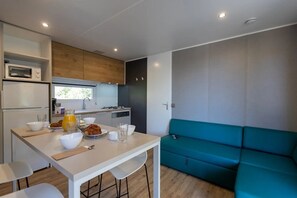 A compact kitchen with a dining area, a teal sofa, and a microwave. - Camping 3 étoiles - Piscine  - ccbgec0 (Pianottoli-Caldarello)