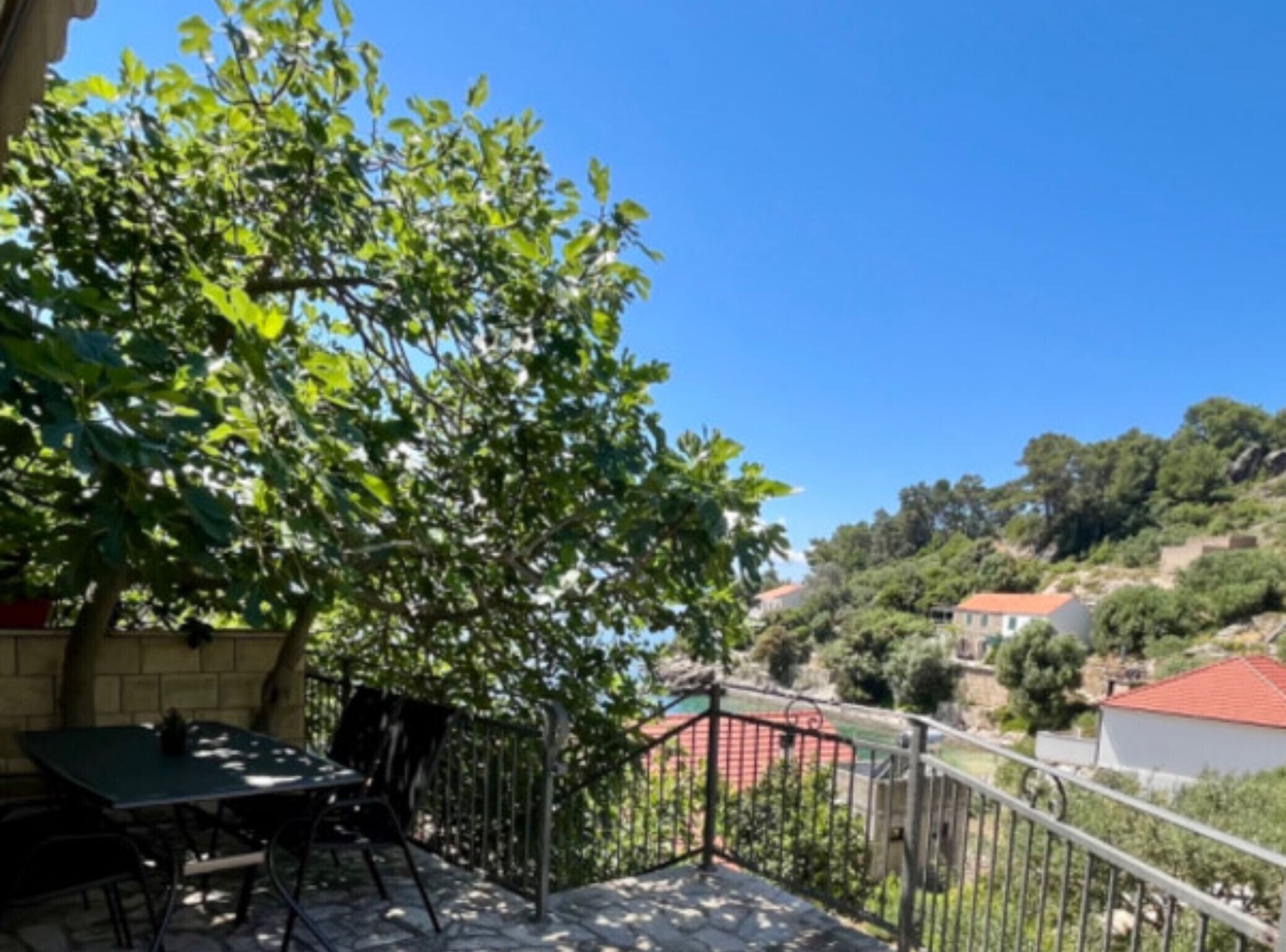 Ein Balkon mit Tisch und Stühlen, ein Baum und Blick auf einen Hang mit Häusern.