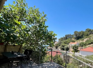 A balcony with a table and chairs, a tree, and a view of a hillside with houses. - Paradise Apartments-Studio apartman with sea view and terrace 2 (Gdinj)