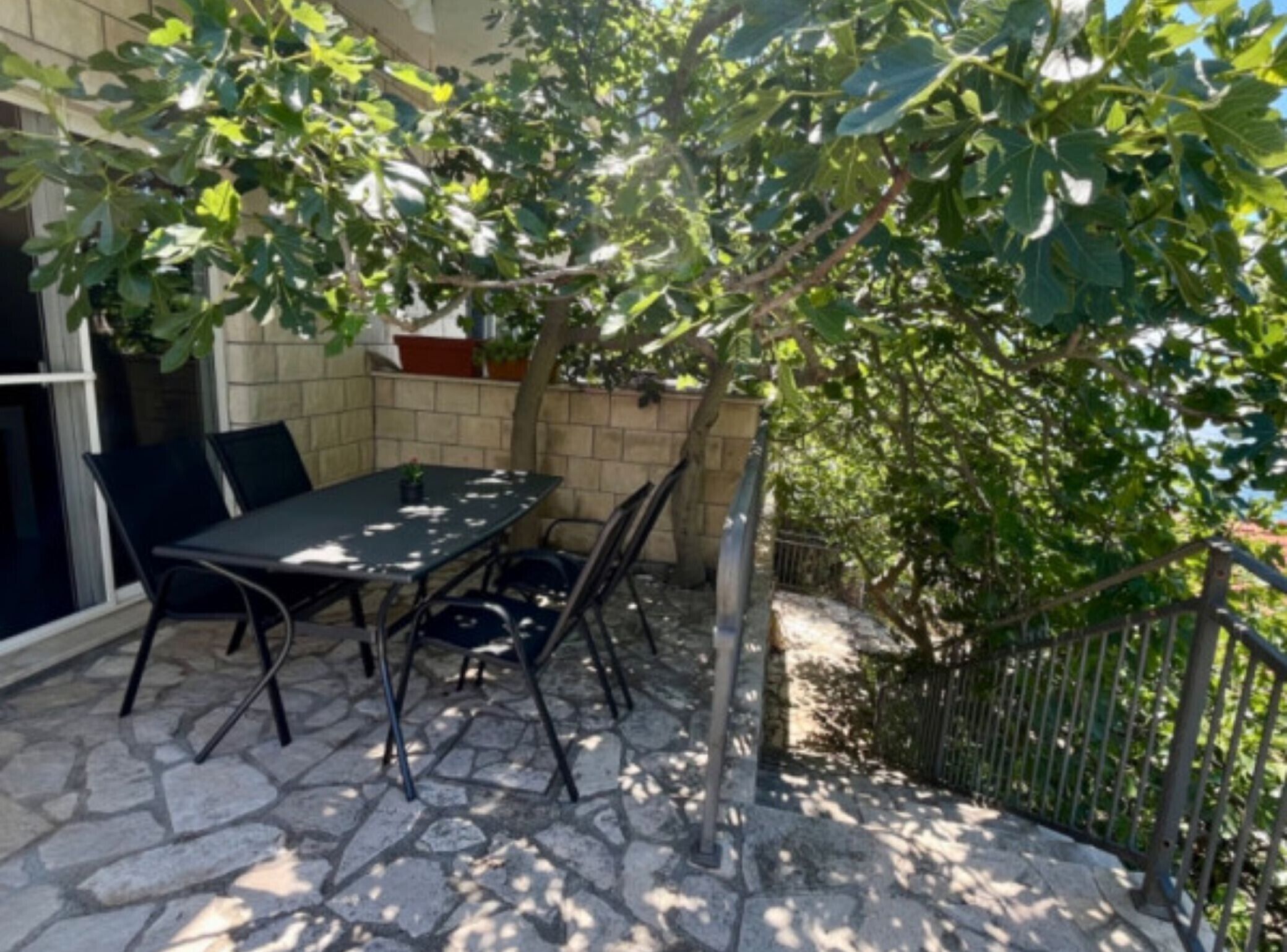 Patio esterno con tavolo e sedie, circondato da pavimento in pietra e vegetazione.