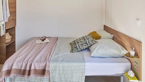 A single bed with a wooden headboard, a bedside table with a lamp, and a wardrobe with hanging clothes. - Camping 3 étoiles - Piscine  - ccbgecb (Pianottoli-Caldarello)