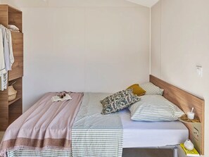 Ein Einzelbett mit Holz-Kopfteil, ein Nachttisch mit Lampe sowie ein Schrank mit Kleidern darin.