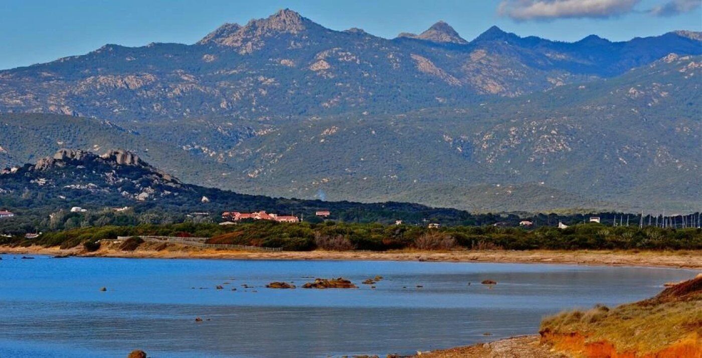 A coastal landscape with mountains, a beach, and a small settlement with buildings.