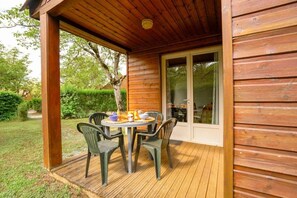 Une terrasse en bois avec une table et des chaises, une porte vitrée donnant sur un espace extérieur et une structure de bâtiment en bois.