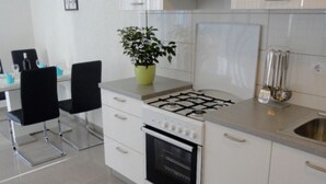 Una cocina moderna con estufa a gas, horno, muebles altos blancos y una zona de comedor con sillas negras.