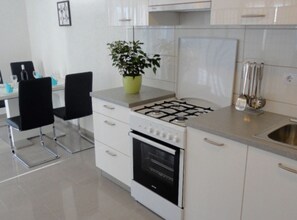 Eine moderne Küche mit Gasherd, Backofen, weißen Schränken und einem Essbereich mit schwarzen Stühlen.