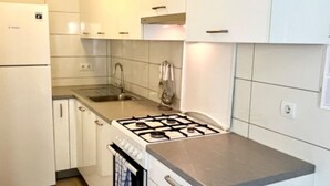 Eine Küche mit weißen Schränken, einer Edelstahl-Arbeitsplatte, einem Gasherd, einer Spüle und einem Kühlschrank.