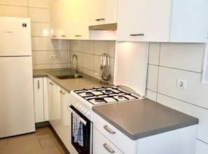 Eine Küche mit weißen Schränken, einer Edelstahl-Arbeitsplatte, einem Gasherd, einer Spüle und einem Kühlschrank.