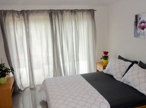 Ein Schlafzimmer mit Bett, Vorhängen, einem Nachttisch mit Pflanze und einem Wandposter.