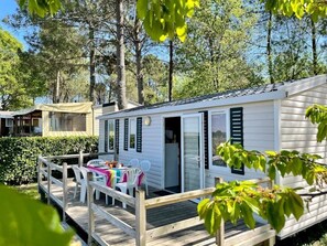 Une maison mobile dotée d’une terrasse, d’un espace salon extérieur et offrant une vue sur la forêt environnante.