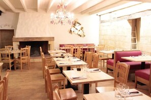 A restaurant with wooden tables and chairs, a chandelier, a fireplace, and a stone wall.