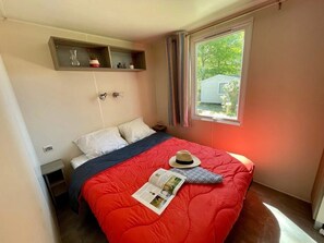 Une chambre à coucher avec un lit, une fenêtre, une étagère ornée d’objets décoratifs et une porte.