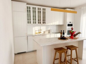 Une cuisine moderne avec des meubles blancs, un plan de travail en marbre et deux tabourets en bois.