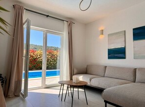 Une pièce avec un canapé, une petite table, un tableau et une vue sur une piscine et un jardin.