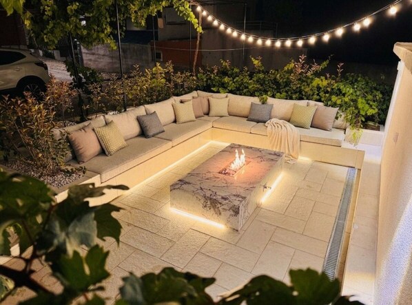Un espace extérieur aménagé avec un foyer, des guirlandes lumineuses et un canapé.