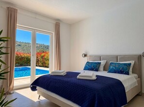 Une chambre à coucher avec un lit, deux oreillers, une fenêtre avec des rideaux et une vue sur une piscine et de la verdure.