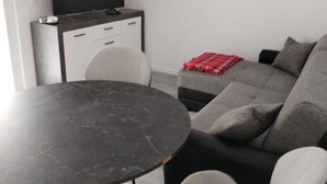 Ein modernes Wohnzimmer mit einem runden Tisch, einer Couch, einem Fernseher und einer kleinen Kommode.