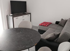 Ein modernes Wohnzimmer mit einem runden Tisch, einer Couch, einem Fernseher und einer kleinen Kommode.