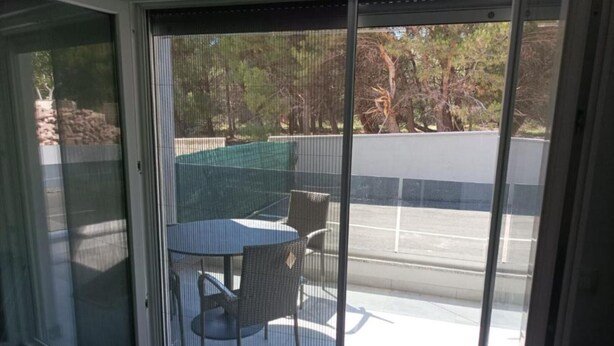 Ein überdachter Patio-Bereich mit Tisch und Stühlen, eine überdachte Sitzgelegenheit und Blick auf einen Parkplatz und Bäume.