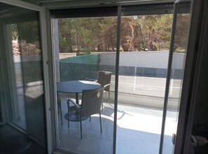 Ein überdachter Patio-Bereich mit Tisch und Stühlen, eine überdachte Sitzgelegenheit und Blick auf einen Parkplatz und Bäume.