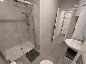 A modern bathroom with a glass-enclosed shower, a white sink, and a door leading to another room. - One Bedroom Apartment with Terrace (Povljana)