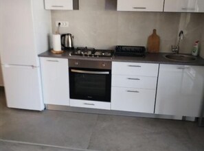 Eine Küche mit Herd, Backofen, Spüle und weißen Schränken.