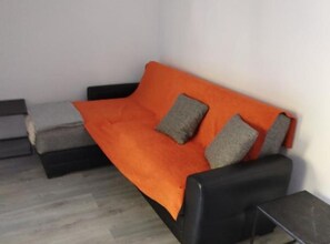 Una stanza con un divano nero, una coperta arancione e due cuscini grigi.